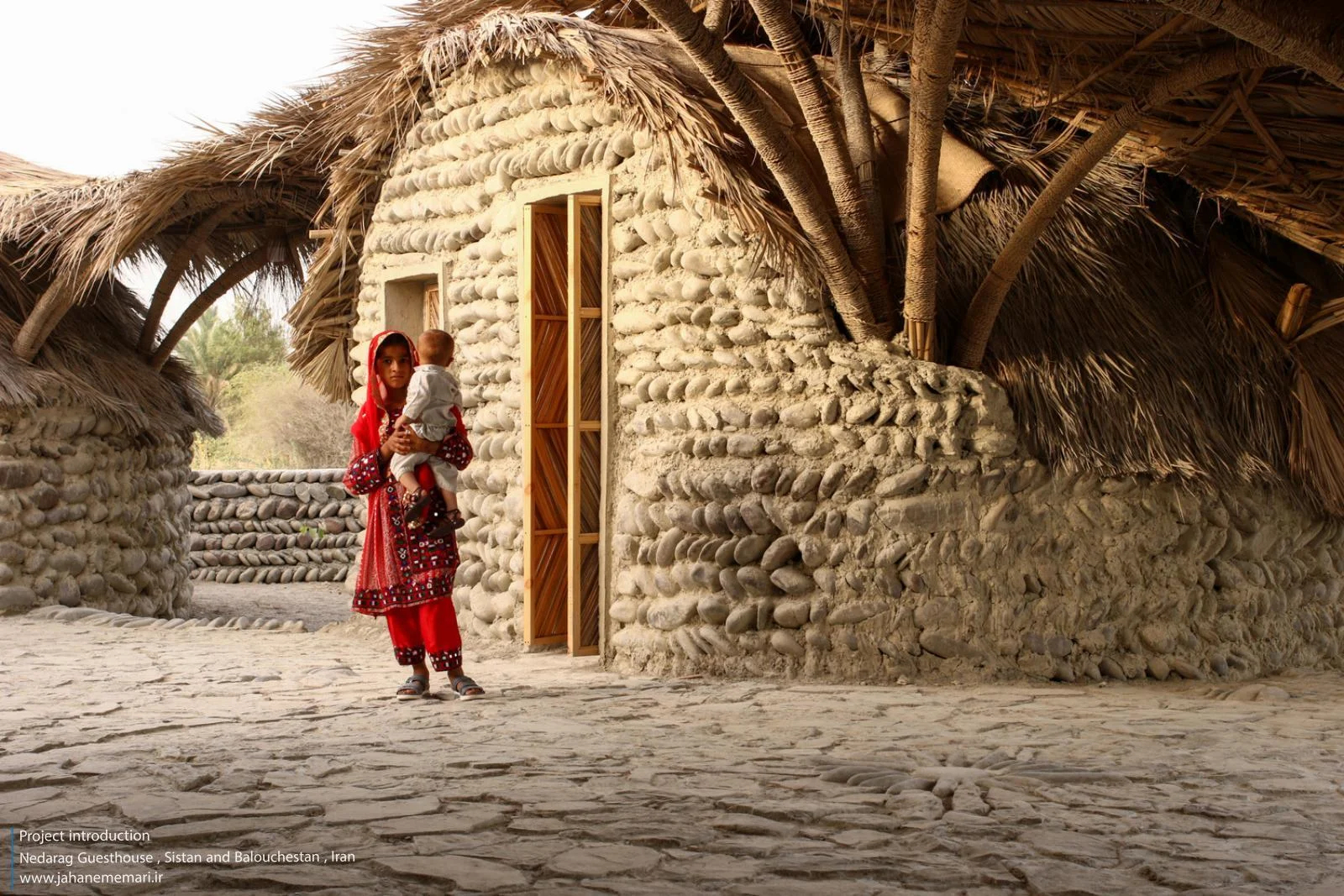نمای خارجی و داخلی مهمانسرای ندارگ در روستای کهنانیکش، سیستان و بلوچستان، که ساختار نیمه‌باز، سقف چتری‌شکل با خرپاهای دست‌ساز و دیوارهای ضخیم گلی آن بر اساس بازتفسیر معماری بومی «کپر» و با هدف خنک‌سازی طبیعی و مشارکت جمعی اهالی طراحی و اجرا شده است.